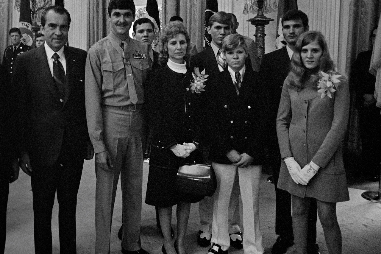Several people pose for a photo. One person wears a military uniform. The others are wearing business attire.