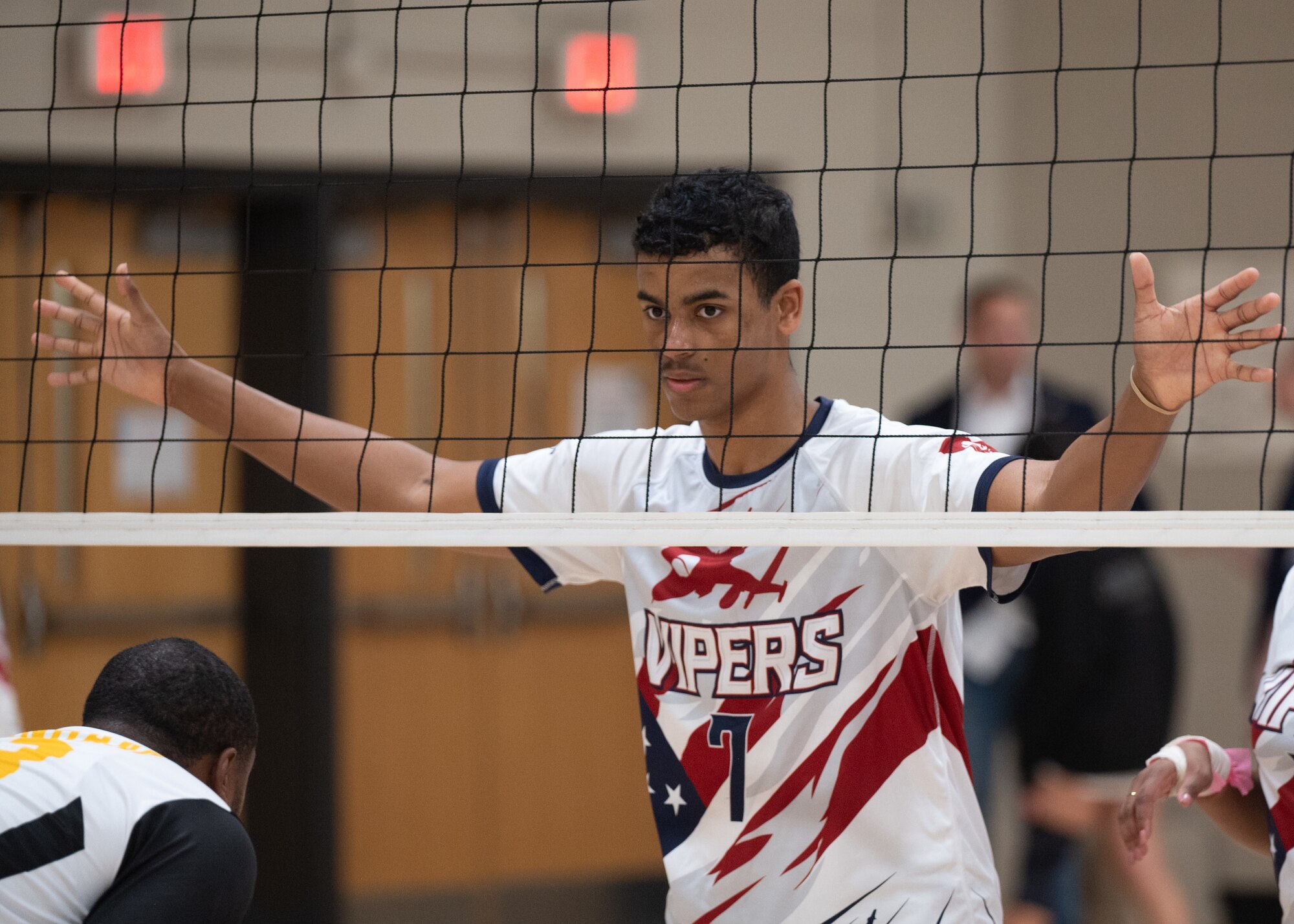 A volleyball player stands on the other side of a net with his arms outstretched