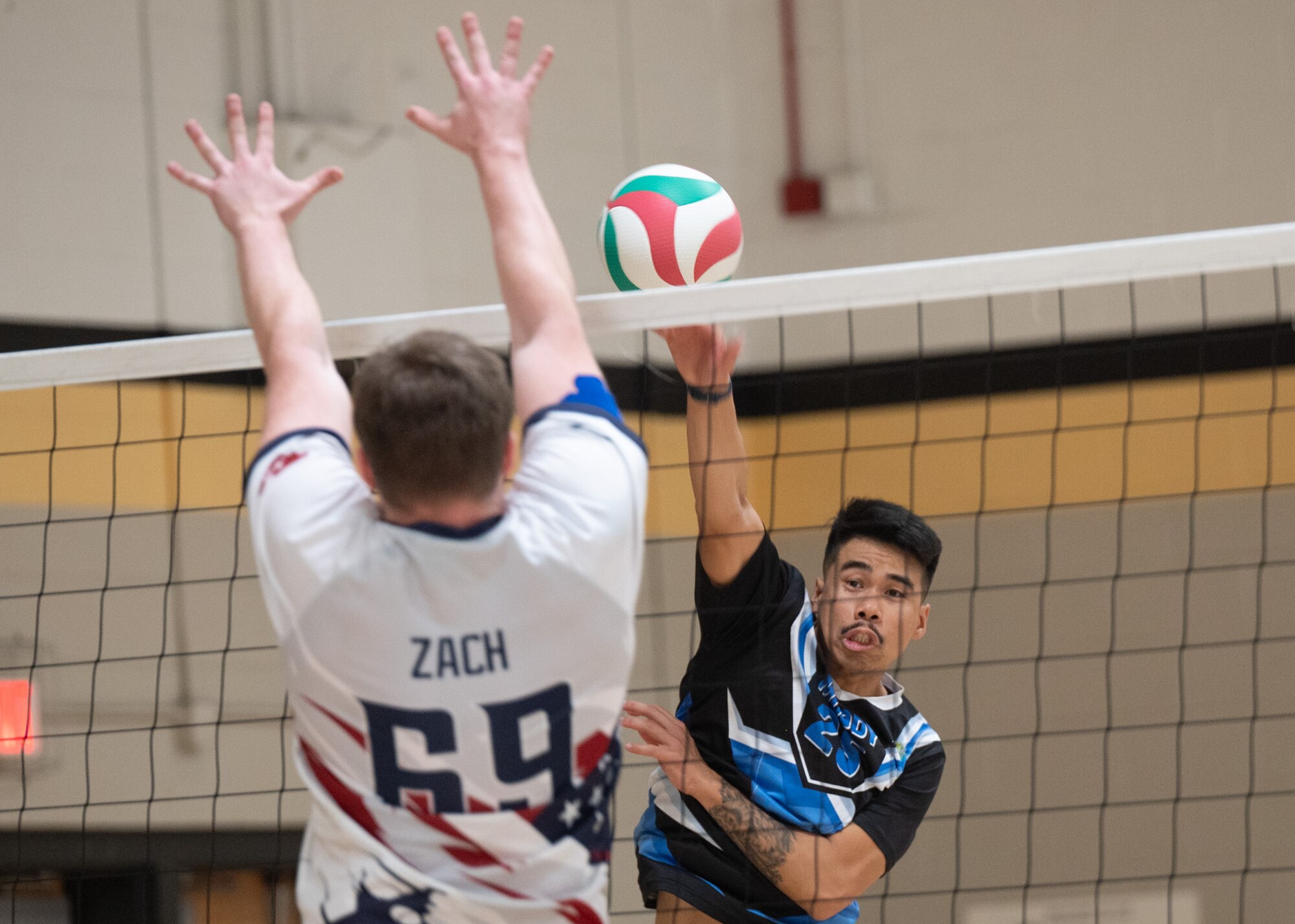 Two volleyball players on opposing teams attempt to spike the ball over the net