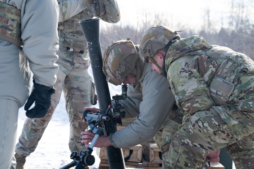 Four soldiers in cold weather gear set up a mortar.