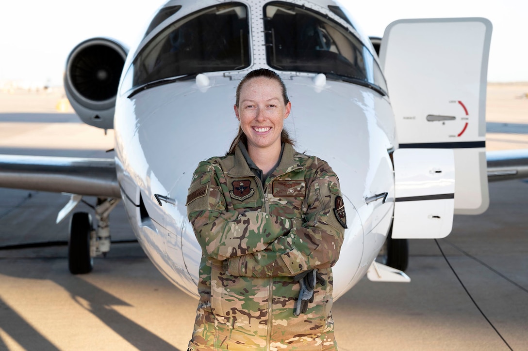 An Air Force pilot smiles while standing in front of an aircraft parked on a flight line.