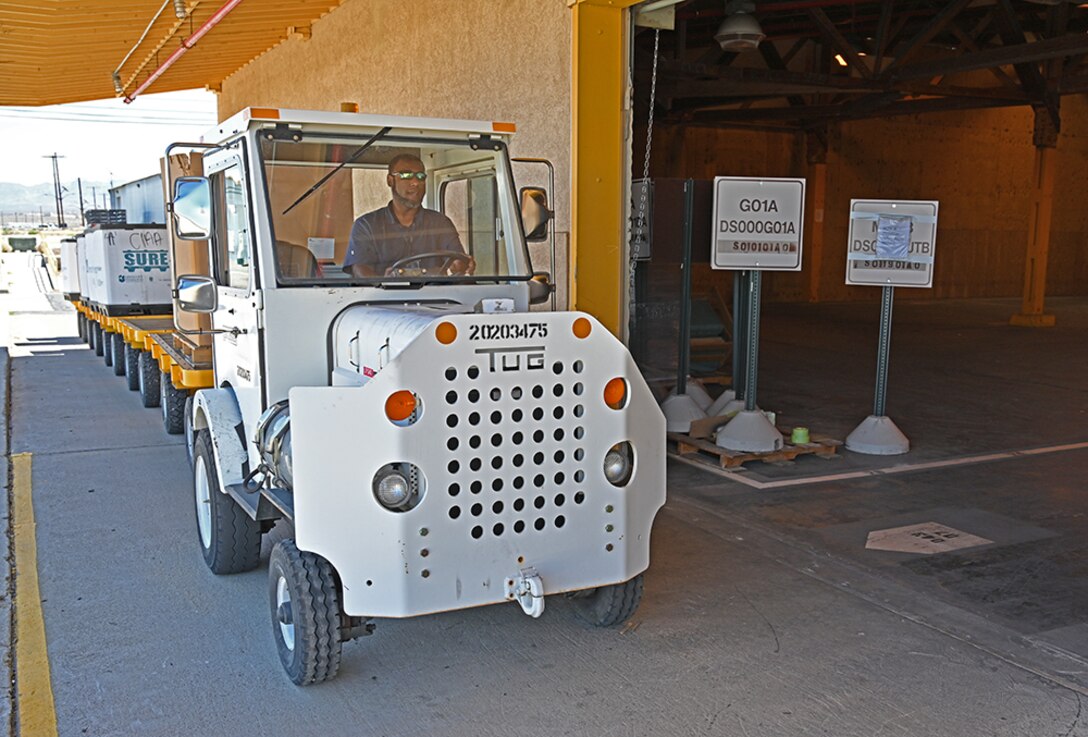 A man operates a freight-pulling tractor outside the open bay door of a warehouse.