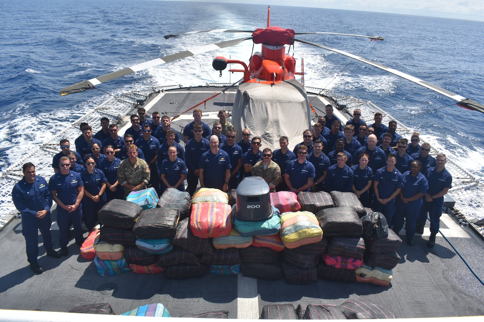 Coast Guard Cutter Resolute crew members take a group photo around $6.2 million worth of marijuana seized during an interdiction on the Eastern Pacific Ocean, Dec. 10, 2023. The Resolute is homeported in St. Petersburg, Florida, and was deployed to the Eastern Pacific Ocean conducting counter narcotics operations in support of Joint Interagency Task Force South.