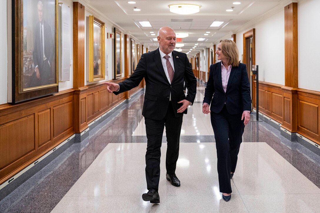 Deputy Defense Secretary Kathleen Hicks walks and talks with another civilian in a hallway.