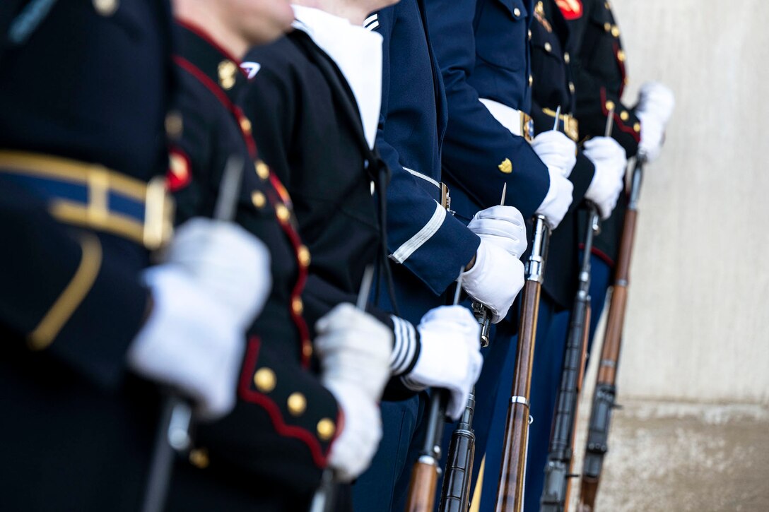 Close-up view of joint service honor guard members in dress uniforms and white gloves standing in a row.