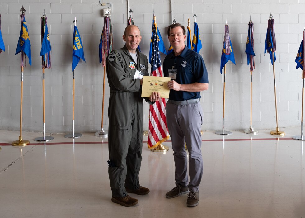 Two people post with a certificate in front of flags