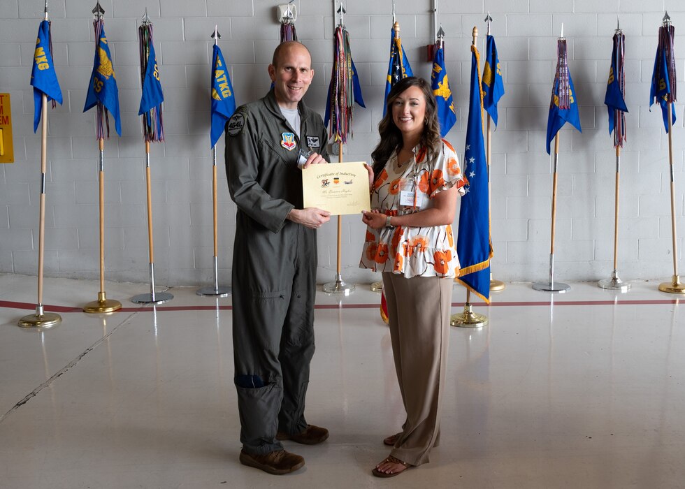 Two people post with a certificate in front of flags