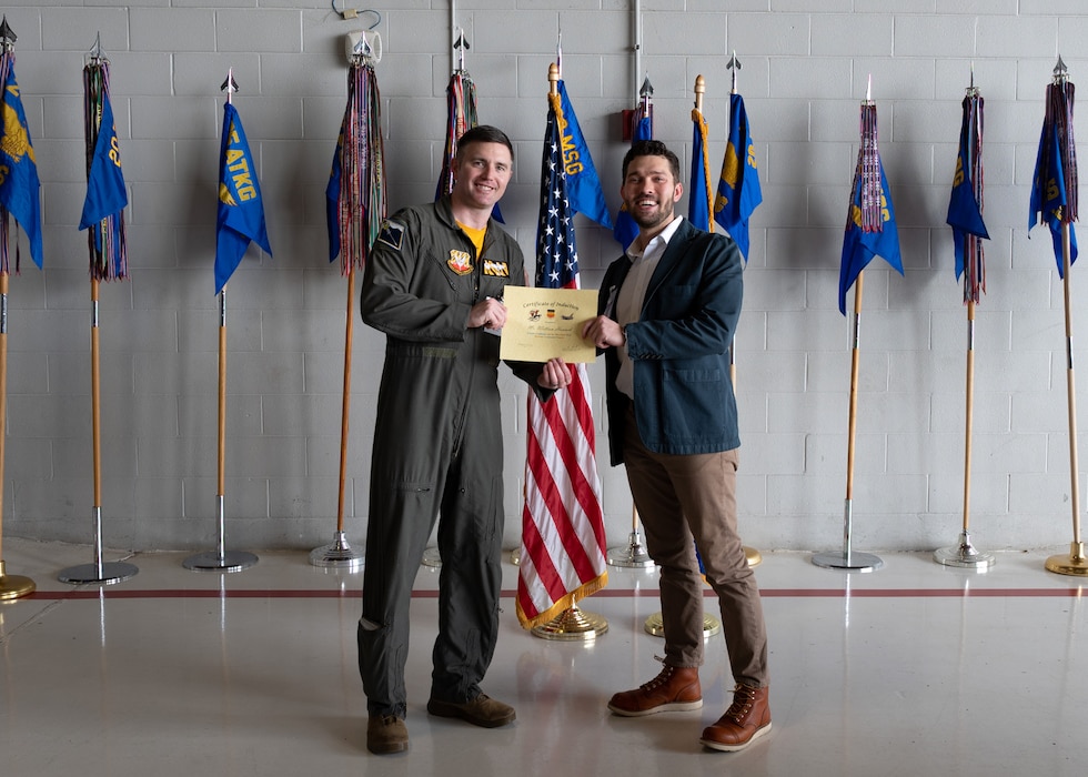 Two people post with a certificate in front of flags