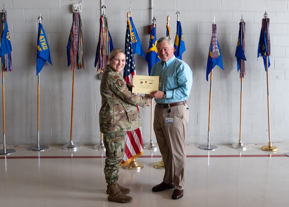 Two people pose with certificates in front of flags