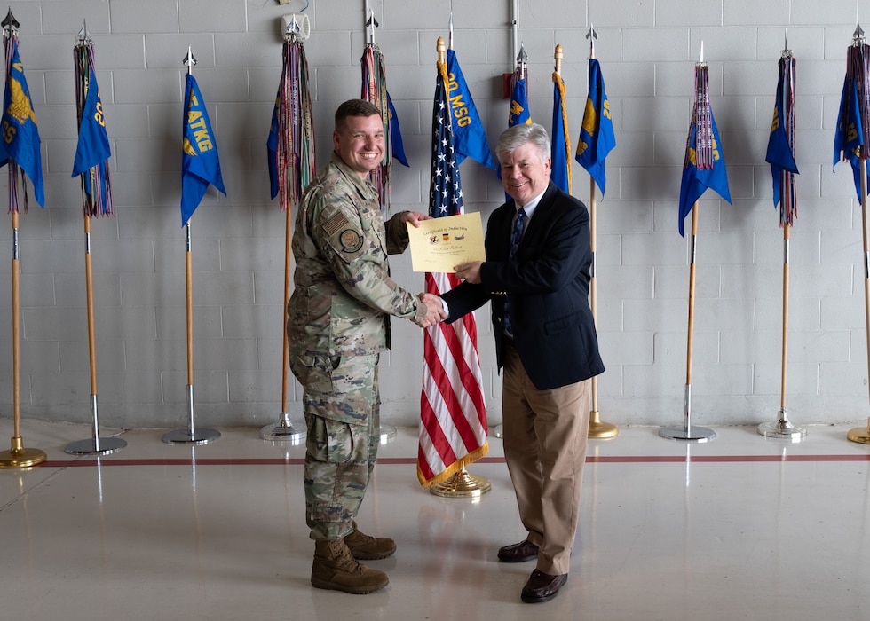 Two people pose with certificates in front of flags