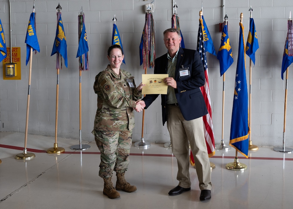 Two people pose with certificates in front of flags