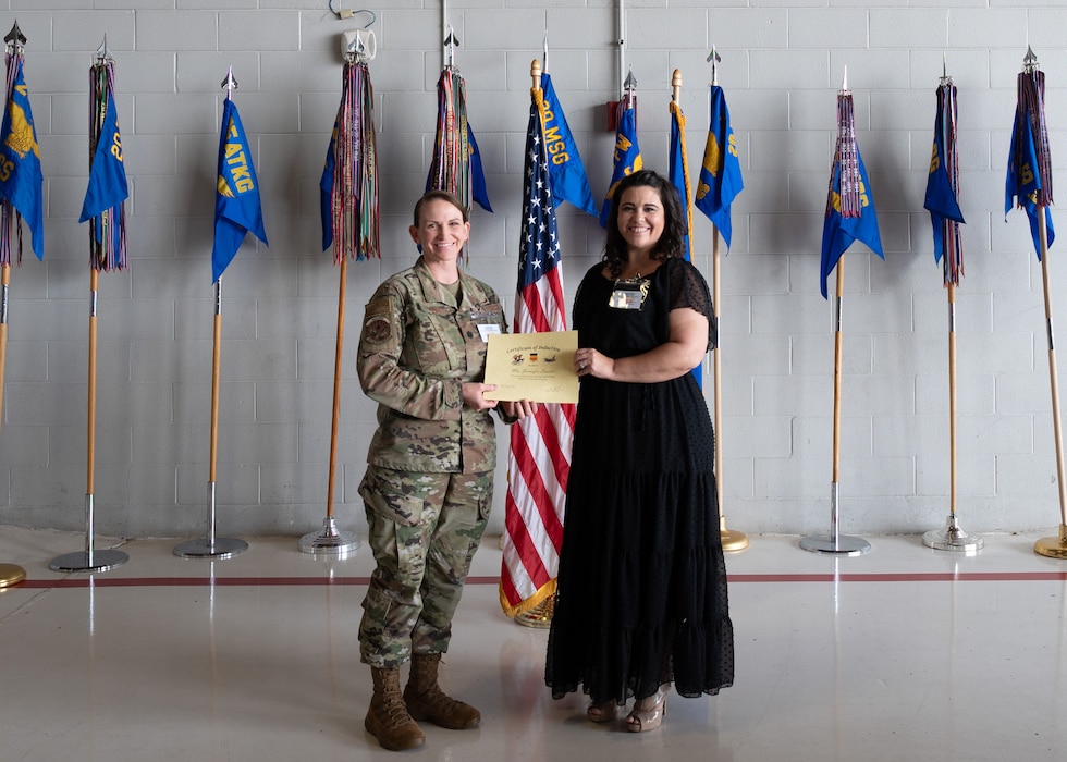 Two people pose with certificates in front of flags