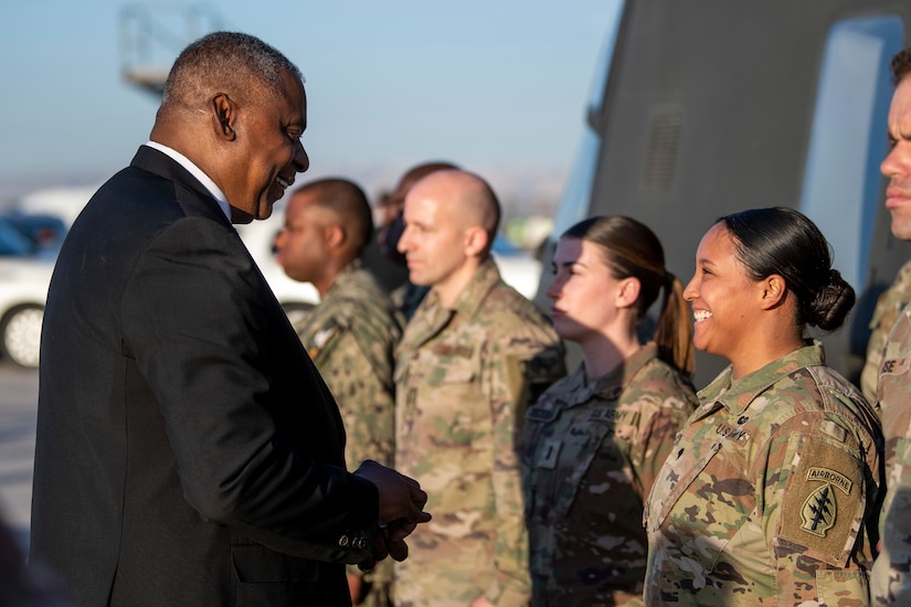 A person in a business suit smiles as he speaks with service members.