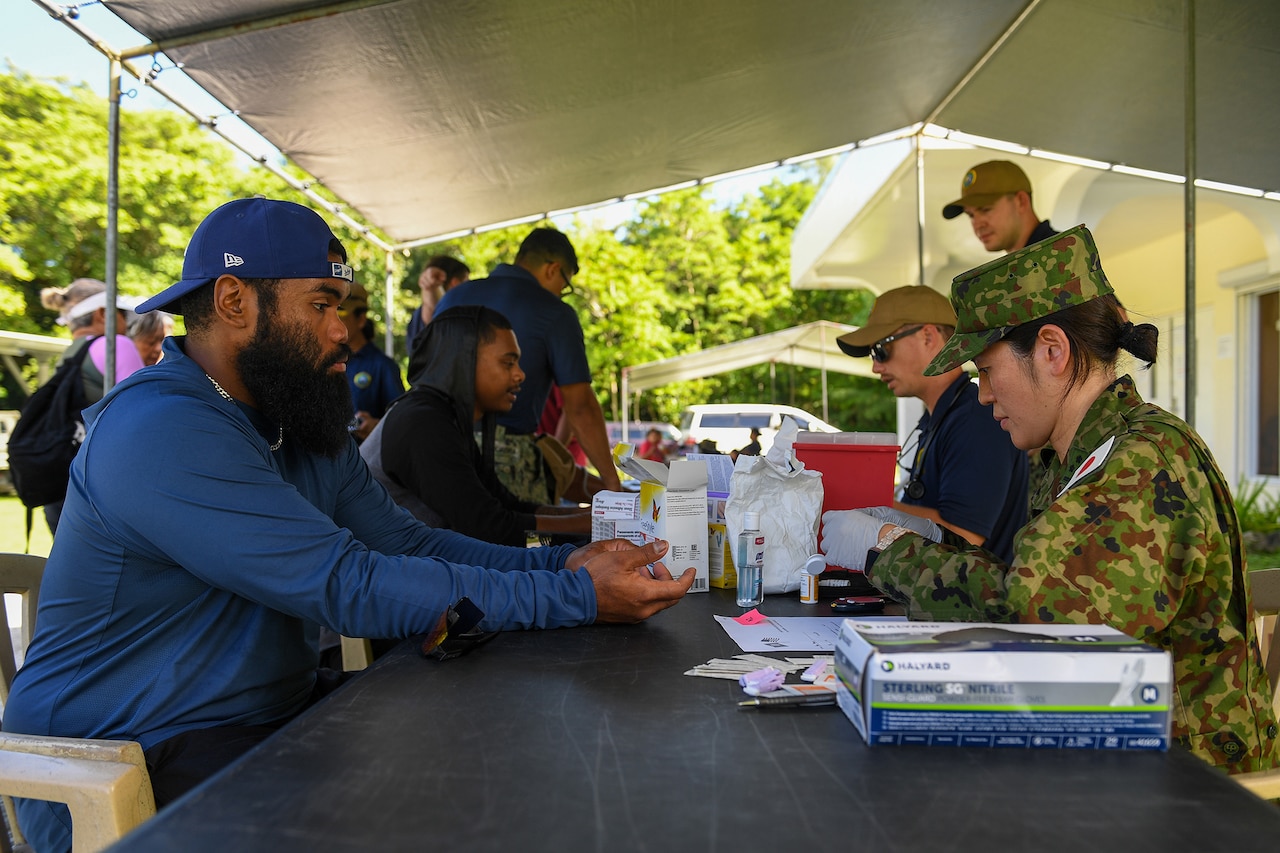 Military and civilians sit at a picnic table.