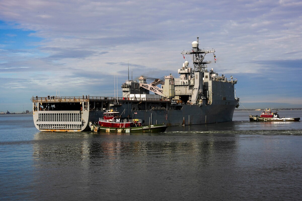 Two tugboats, perpendicular to a larger ship, pull it in open waters.