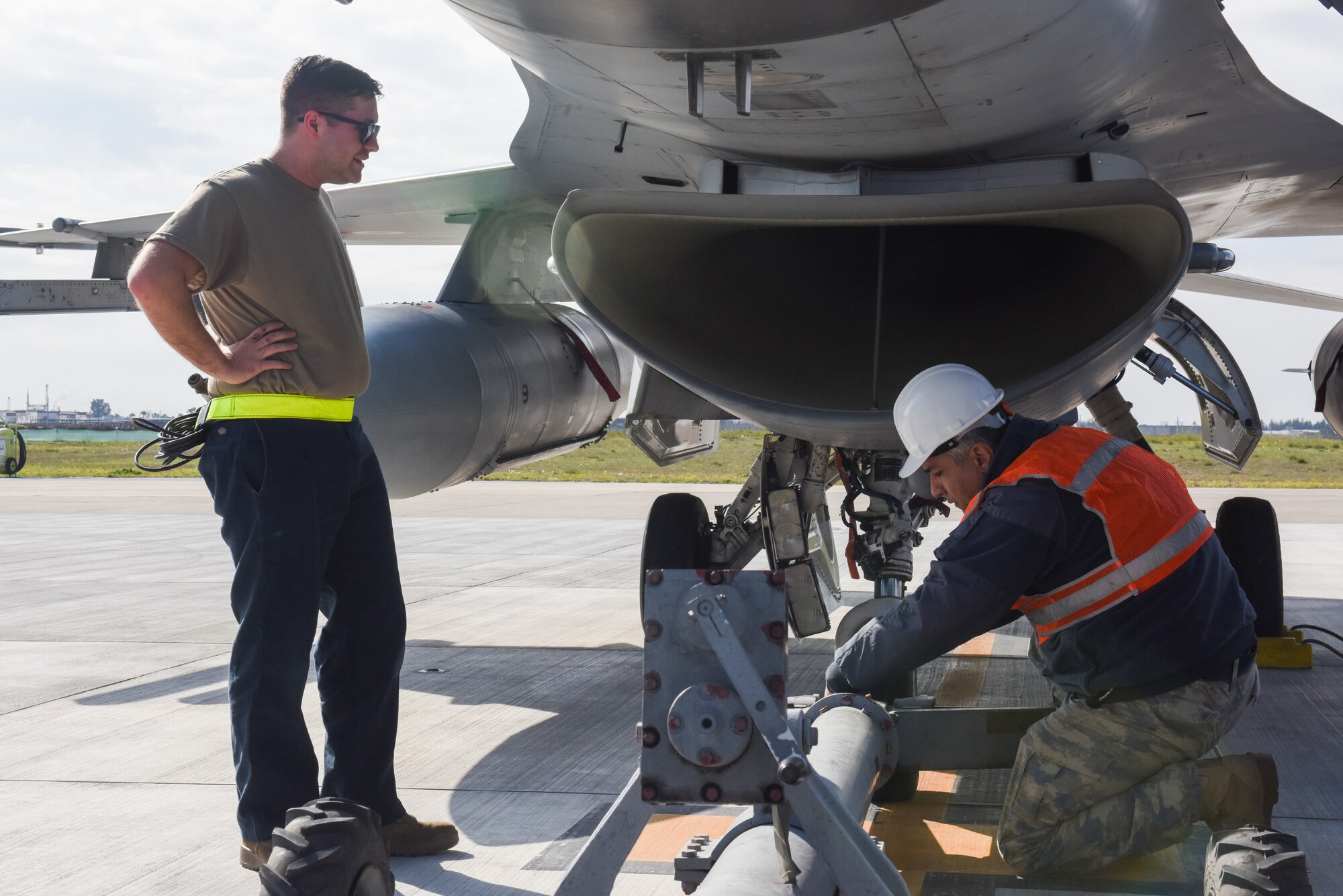 Turkish and American military members connect a tow bar to an F16 fighter jet