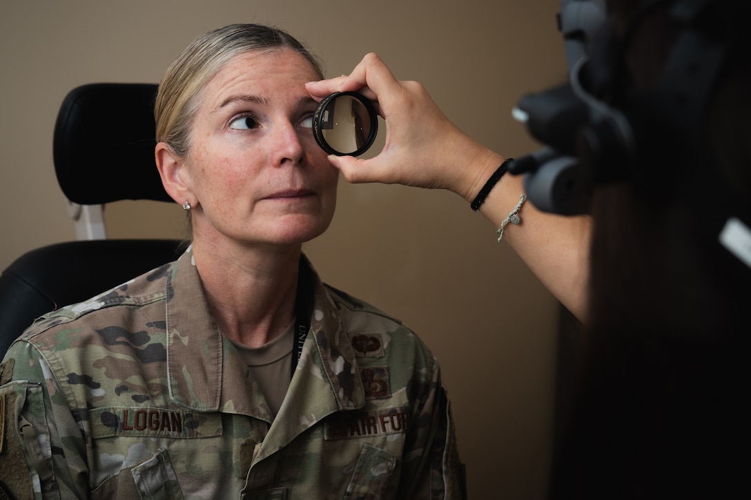 A physician holds a magnifying lens in front of a service member’s eye during a vision exam.