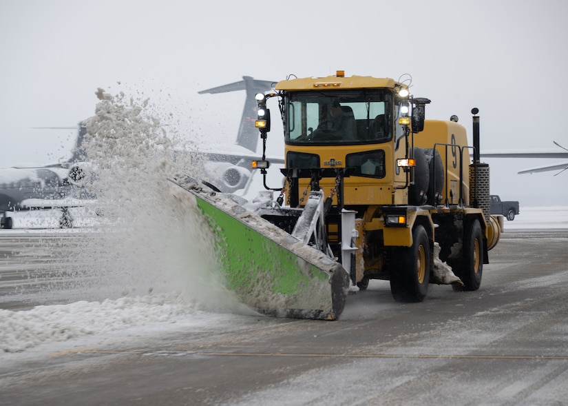 Yellow snow plow plows snow off of the flight line.