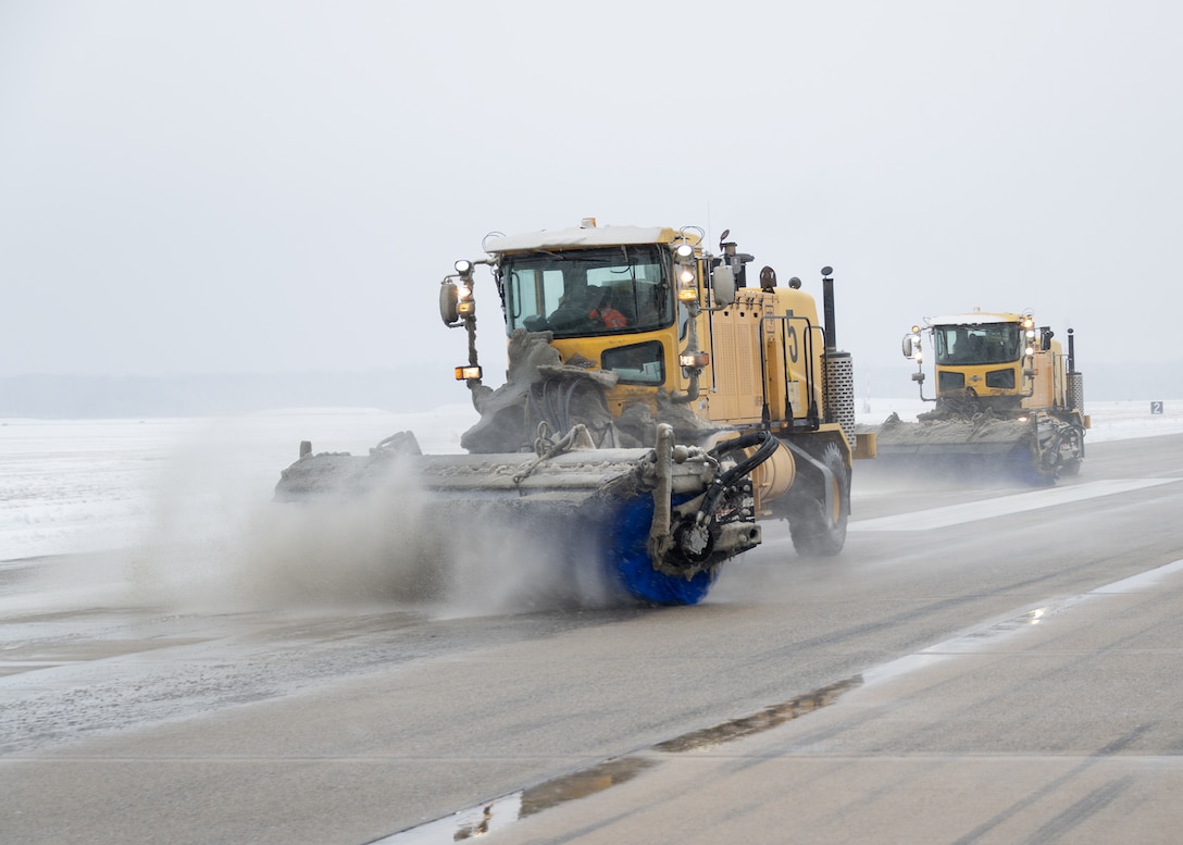 Yellow truck sweeps ice and snow off of flight line.