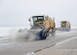Yellow truck sweeps ice and snow off of flight line.