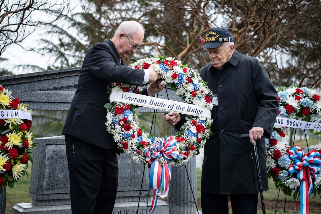 A veteran helps place a wreath at a memorial in a cemetery.