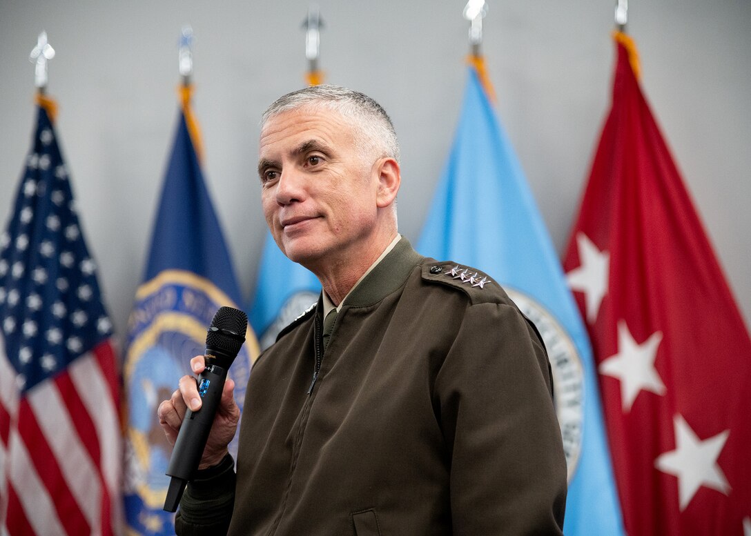 General Nakasone stands in front of flags to address the workforce.