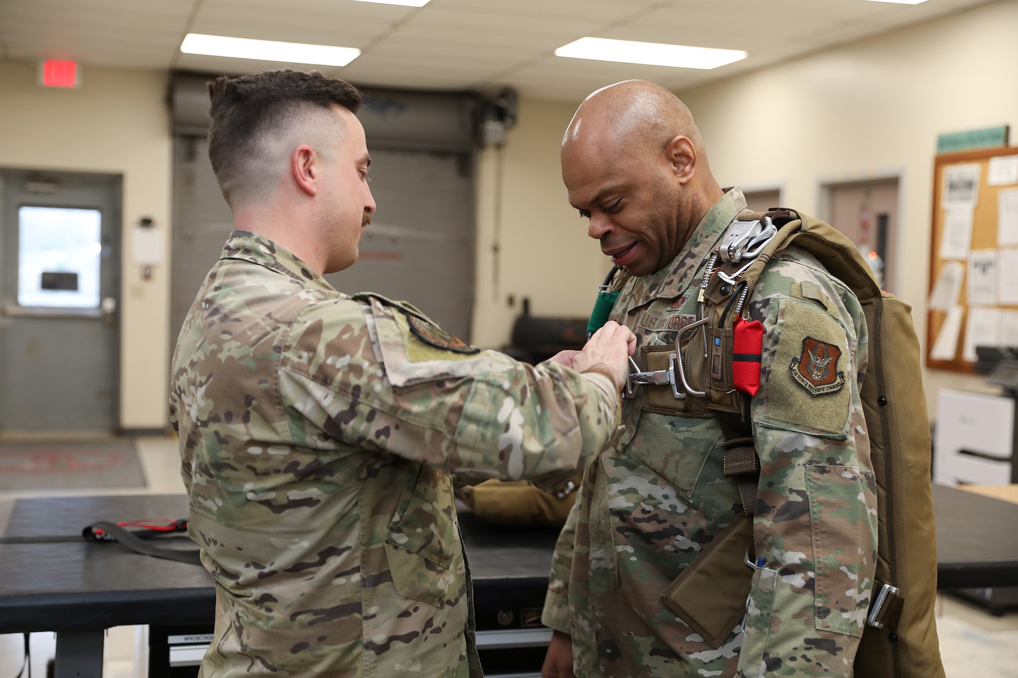 Tech. Sgt. Nathan Pritchard, 445th Operations Support Squadron Survival, Evasion, Resistance and Escape (SERE) instructor, helps Chief Master Sgt. Travon W. Dennis, Fourth Air Force Command Chief, March Air Reserve Base, California, try on a parachute during his visit with 445th OSS Airmen Jan. 7, 2024. Chief Dennis visited the 445th Airlift Wing Jan. 6-7, 2024 and met with Airmen from various squadrons and the 445th Development and Training Flight, he toured the 445th Aeromedical Staging Squadron simulation lab, participated in an aircrew flight equipment demonstration and was briefed on the security forces weapons simulator training. Chief Dennis also met with the 445th's Chief’s Group, Rising Six and First Sergeant Council. (U.S. Air Force photo/Senior Airman Angela Jackson)