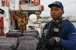 A crew member of the Coast Guard Cutter Resolute stands watch over illegal narcotics, Jan. 29, 2024, in St. Petersburg, FL. Armed Coast Guardsmen stand watch over interdicted drugs to ensure security and accountability of seized contraband. (U.S. Coast Guard photo by Petty Officer 3rd Class Nicholas Strasburg)