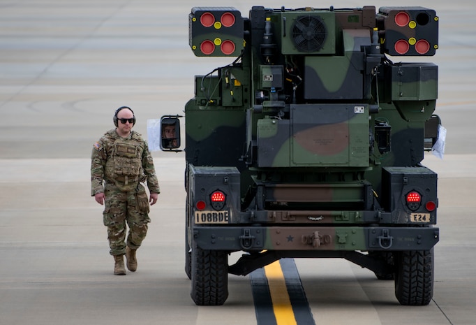 A photo of an Airman walking guiding a vehicle.