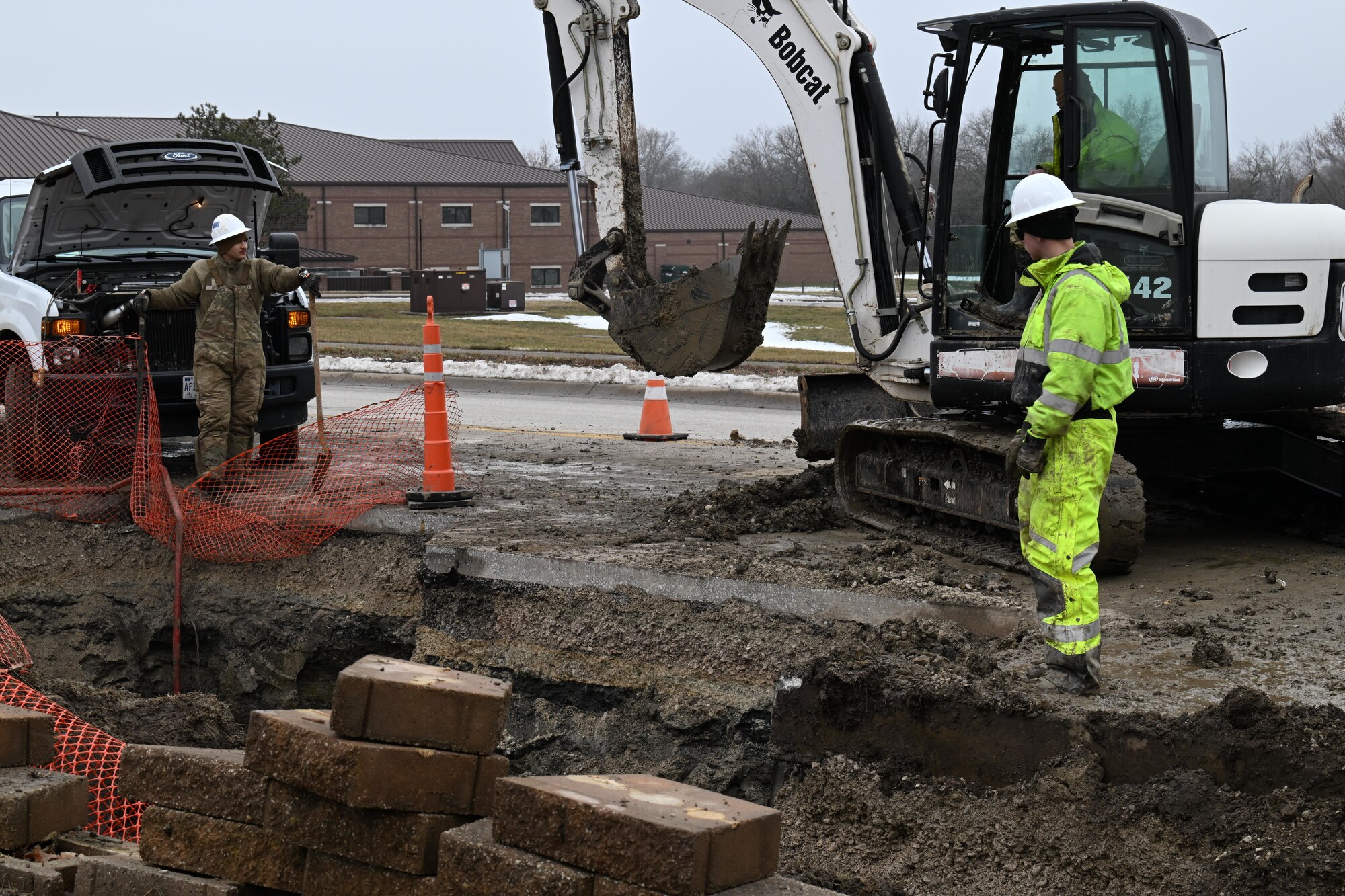 U.S. Airmen assigned to the 509th Civil Engineer Squadron work together to excavate dirt and pieces of road away from a burst water main at Whiteman Air Force Base, Mo., Jan 25, 2024. To repair the water main, equipment operators need to cut away pieces of road and move dirt away from the site so plumbers can repair the pipe. (U.S. Air Force photo by Airman 1st Class Matthew S. Domingos)