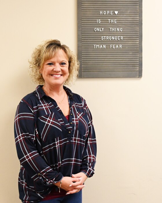 Image of Noni New in her office in front a of wooden wall sign.