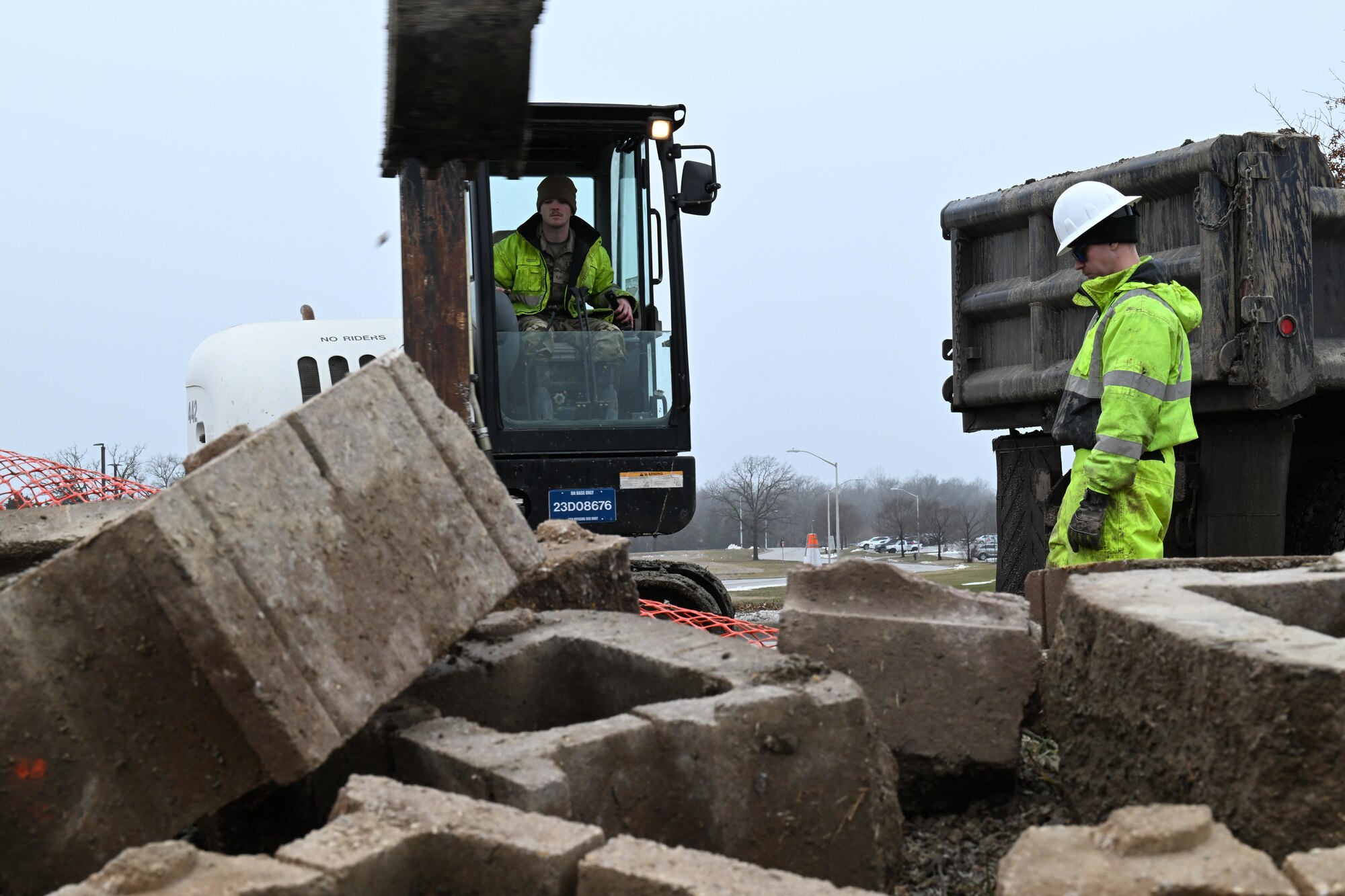 U.S. Air Force Senior Airman Eric Neely, left, and Senior Airman Ethan Brill, 509th Civil Engineer Squadron heavy equipment operators, excavate dirt from under Spirit Blvd. at Whiteman Air Force Base, Mo., Jan 25, 2024. The water main under Spirit Blvd. burst causing dangerous conditions and potential damage. (U.S. Air Force photo by Airman 1st Class Matthew S. Domingos)