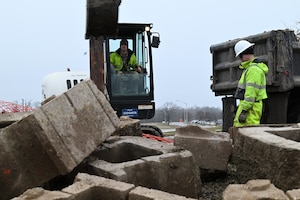 U.S. Air Force Senior Airman Eric Neely, left, and Senior Airman Ethan Brill, 509th Civil Engineer Squadron heavy equipment operators, excavate dirt from under Spirit Blvd. at Whiteman Air Force Base, Mo., Jan 25, 2024. The water main under Spirit Blvd. burst causing dangerous conditions and potential damage. (U.S. Air Force photo by Airman 1st Class Matthew S. Domingos)