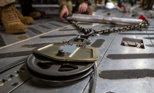 A close up shot of a pulley system lying on the floor of a C-17 being prepared to offload an HH-60W.