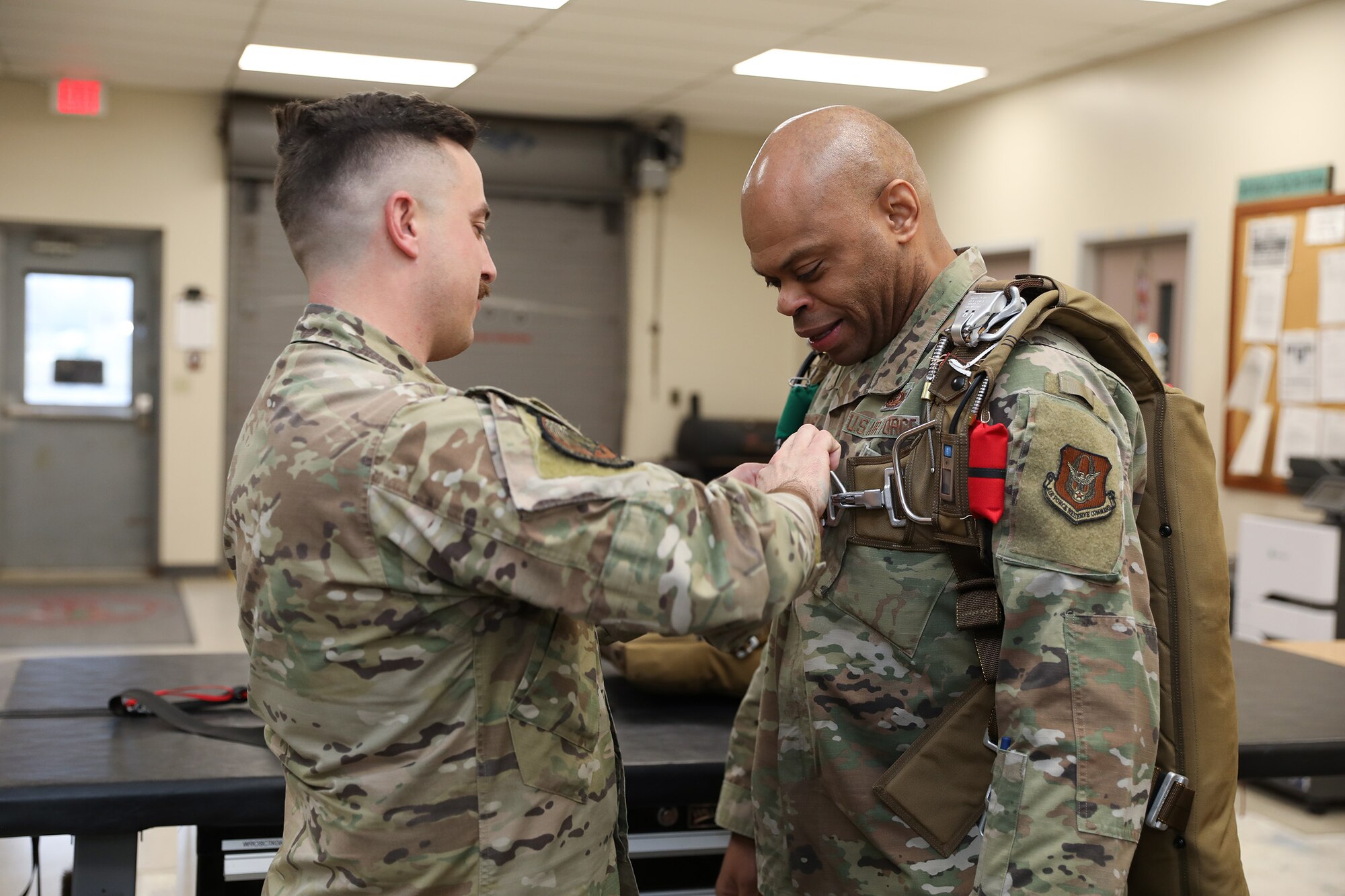 Tech. Sgt. Nathan Pritchard, 445th Operations Support Squadron Survival, Evasion, Resistance and Escape (SERE) instructor, helps Chief Master Sgt. Travon W. Dennis, Fourth Air Force Command Chief, March Air Reserve Base, California, try on a parachute during his visit with 445th OSS Airmen Jan. 7, 2024. Chief Dennis visited the 445th Airlift Wing Jan. 6-7, 2024 and met with Airmen from various squadrons and the 445th Development and Training Flight, he toured the 445th Aeromedical Staging Squadron simulation lab, participated in an aircrew flight equipment demonstration and was briefed on the security forces weapons simulator training. Chief Dennis also met with the 445th's Chief’s Group, Rising Six and First Sergeant Council. (U.S. Air Force photo/Senior Airman Angela Jackson)
