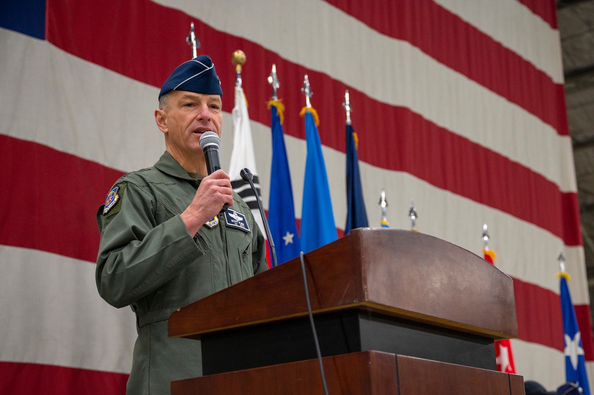 U.S. Air Force Lt. Gen. Scott Pleus, outgoing Seventh Air Force commander, speaks during the Seventh Air Force change of command ceremony behind a podium, in front of a large flag background.