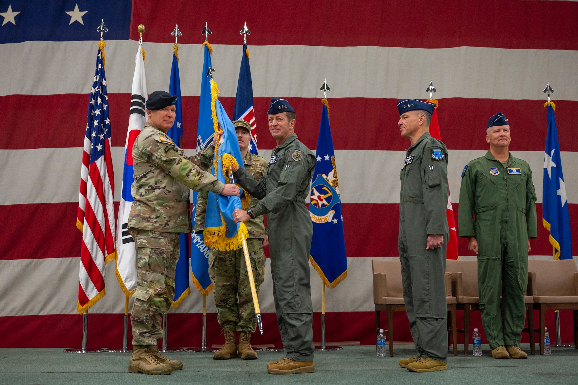 U.S. Army Gen. Paul LaCamera, United Nations Command, ROK-U.S. Combined Forces Command and United States Forces Korea commander, presents the guidon to U.S. Air Force Lt. Gen. David Iverson, incoming Seventh Air Force commander at Osan Air Base, Republic of Korea, on a stage in front of a flag.