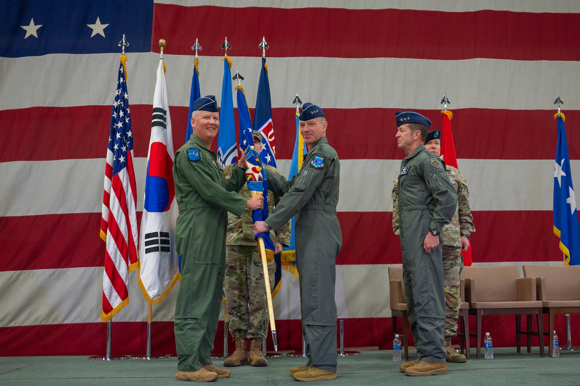 U.S. Air Force Lt. Gen. James Jacobson, Headquarters Pacific Air Forces deputy commander, receives the guidon from U.S. Air Force Lt. Gen. Scott Pleus, outgoing Seventh Air Force commander, in front of a flag on a stage at the Seventh Air Force change of command ceremony at Osan Air Base, Republic of Korea.