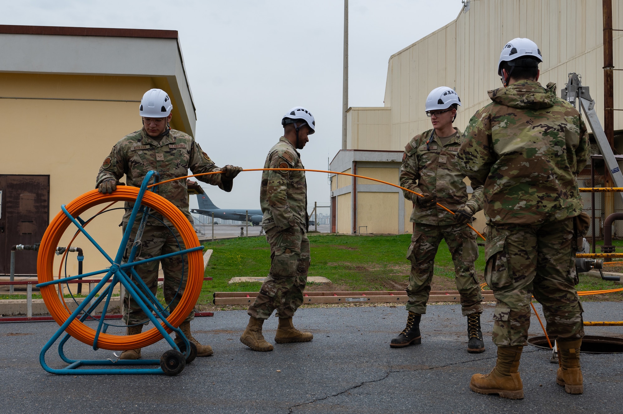 Multiple Airmen pull duct rod into a manhole.