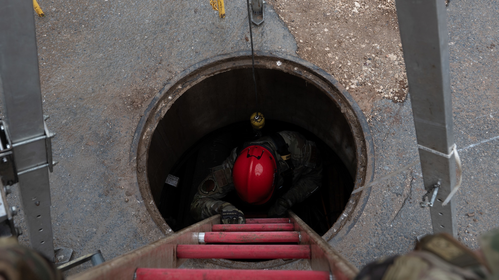 An airman climbs down a ladder in a manhole.