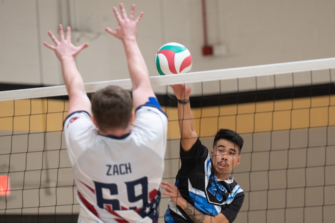An airman's arms are raised to block a volleyball from coming over the net.