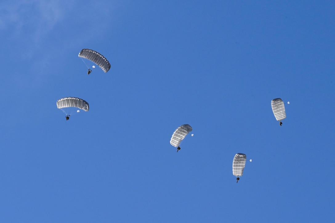 Five airmen conduct a parachute jump against a blue sky.