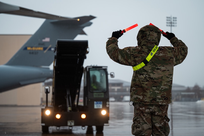 A U.S. Air Force Airman assigned to the 305th Aerial Port Squadron signals stairs for aircraft at Joint Base McGuire-Dix-Lakehurst, N.J., Jan. 25, 2024. More than 1,500 New Jersey Army National Guard Soldiers are deploying to support U.S. Central Command’s Combined Joint Task Force-Operation Inherent Resolve. This is the largest deployment of NJARNG Soldiers since 2008. (U.S. Air Force photo by Senior Airman Sergio Avalos)