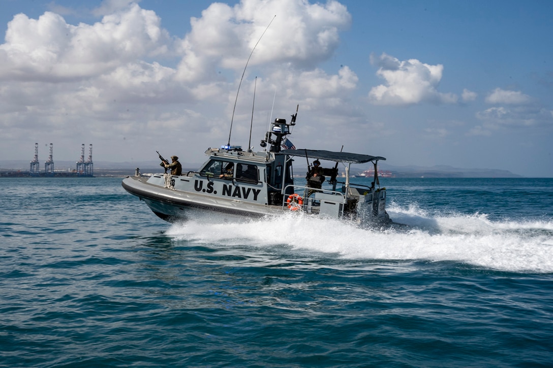 Sailors hold weapons while riding in a patrol boat in open water during daylight.