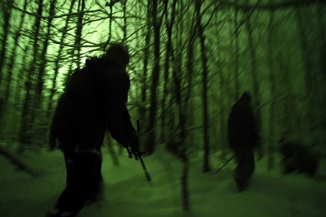 Two soldiers walk in a wooded area with snow on the ground. They are illuminated by a green flare.