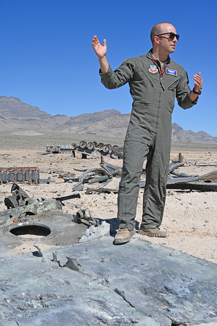 A military officer stands on a piece of exploded vehicle in the desert.