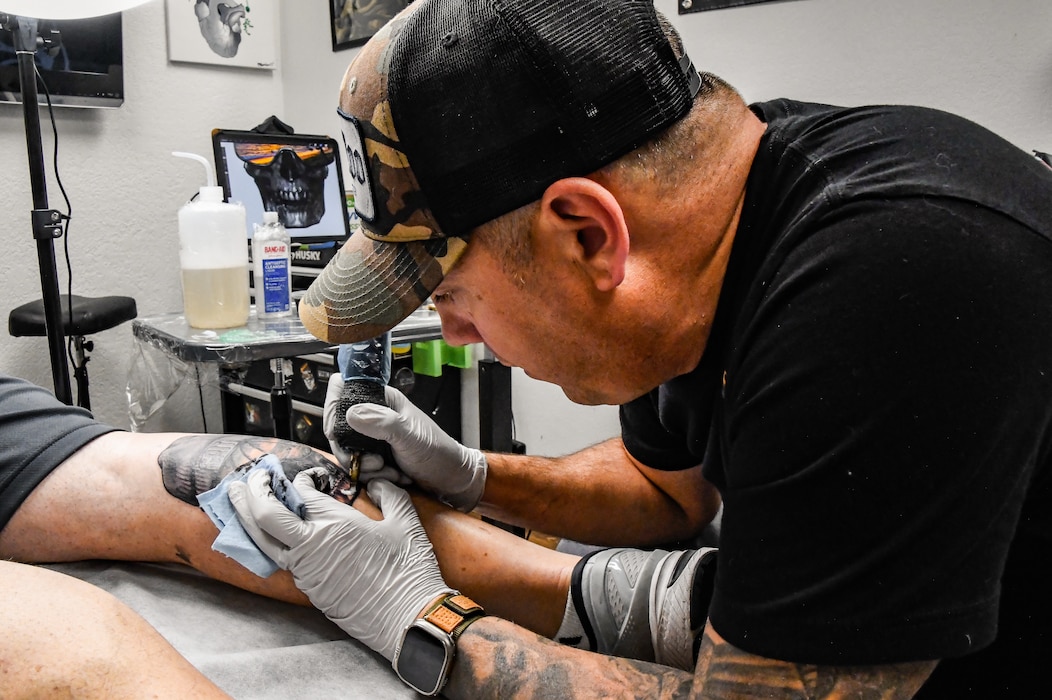 U.S. Air Force Chief Master Sgt. George Bender, 168th Aircraft Maintenance Squadron Chief, tattoos Brian Dianoski, Fairbanks resident, at Sublime Line Tattoo shop in Fairbanks, Alaska, Sept. 27, 2023. The word GRIT was part of the art piece and stands for determination and courage to push through any challenge or obstacle with guts, resilience, initiative, and tenacity. Bender serves as a Chief Master Sgt. in the 168th Wing, 168th Aircraft Maintenance Squadron in the Alaska Air National Guard at Eielson Air Force Base, and during his off-duty hours away from the unit, he delves into his love and passion for art as a professional tattoo artist in Fairbanks, Alaska. Over the years, Bender has drawn and developed designs for the KC-135 Stratotanker nose art, unit patches, and various projects for unit organizations such as Top 3. His art is currently on the Maintenance Group unit patch worn on the shoulders of all the MXG members, representing their pride in their maintenance craftsmanship. (U.S. Air National Guard photo by Senior Master Sgt. Julie Avey)