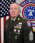 U.S. Army Soldier in dress uniforms poses before an American Flag and a USAREC Flag