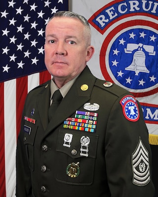 U.S. Army Soldier in dress uniforms poses before an American Flag and a USAREC Flag