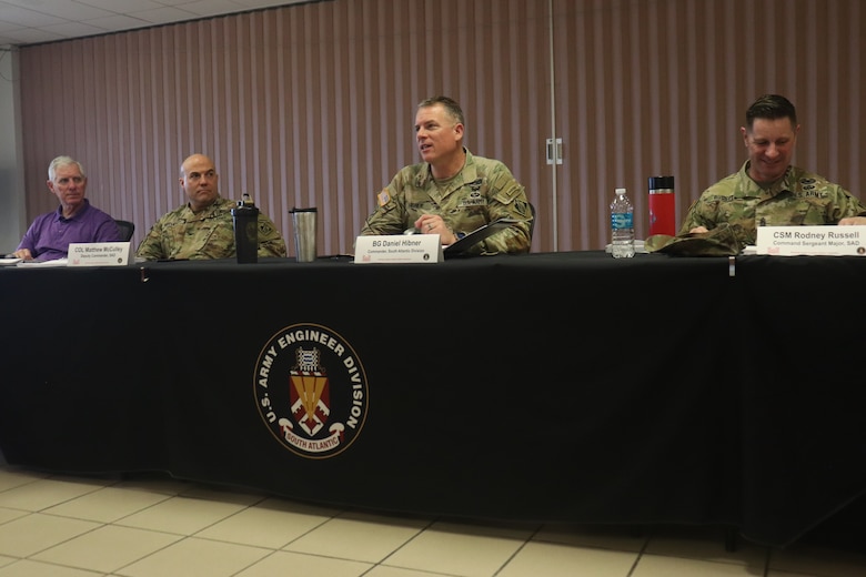 Brig. Gen. Daniel Hibner seated with 2 soldiers in uniform and a civilian at a table covered in black tablecloth.